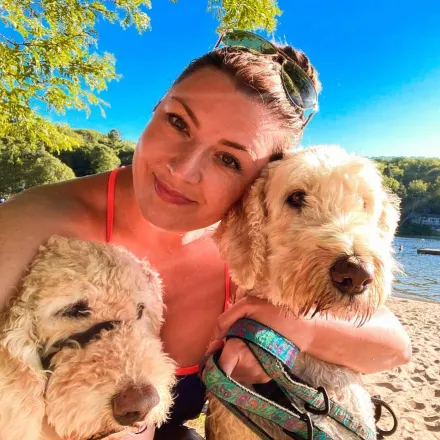 Dr. Natalie Reid cuddling with two beige dogs on a beach